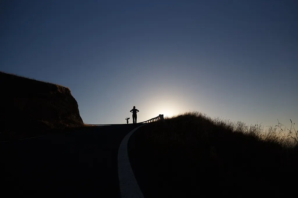 Silhouette mains sur les hanches au sommet d'une route de colline, face au soleil levant