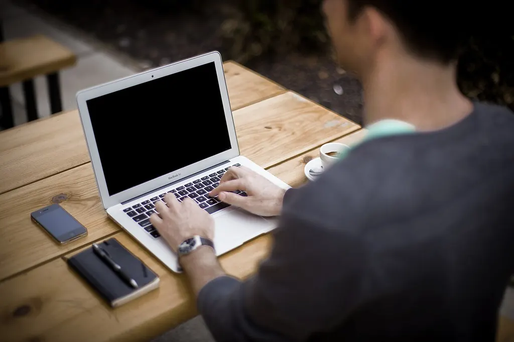 Homme qui travaille sur son ordinateur portable à une table en bois, téléphone et carnet à portée de main