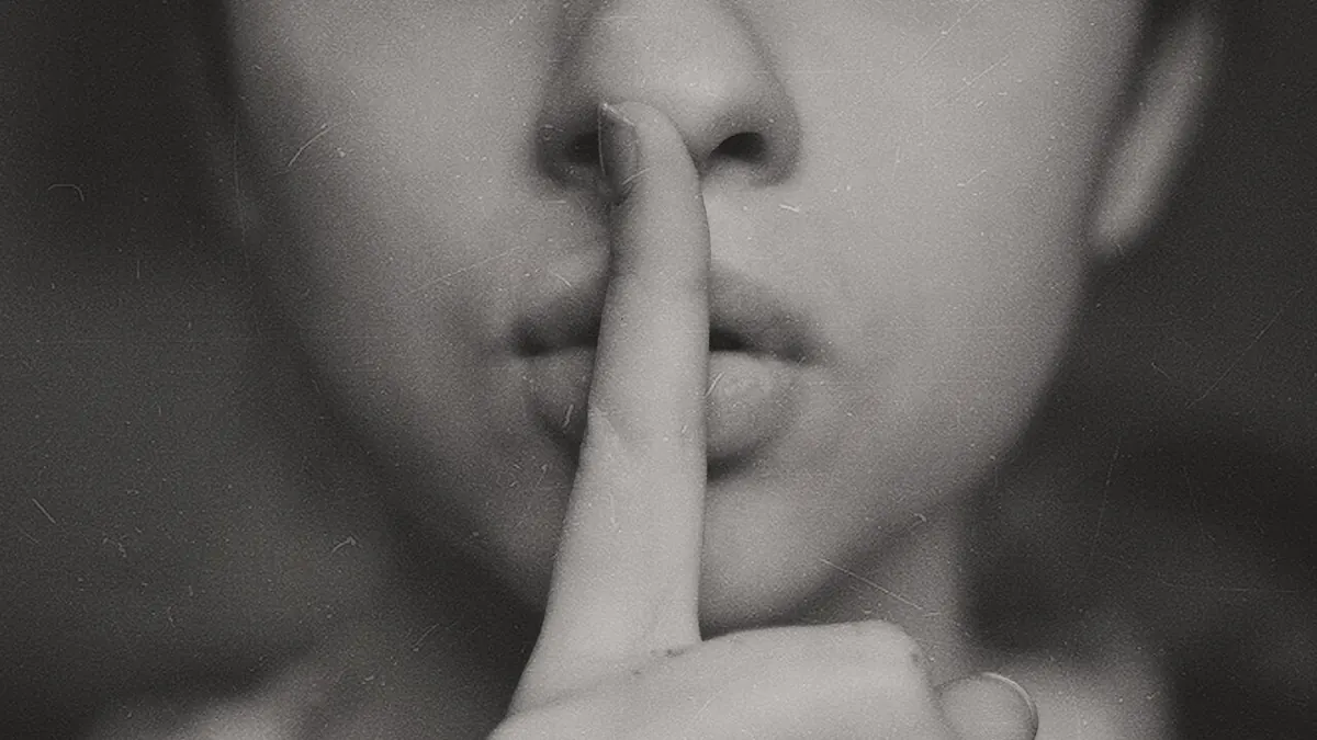 Gros plan sur un visage dont l'index est posé sur les lèvres, en noir et blanc