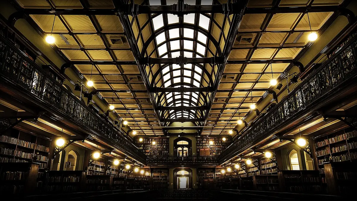 Grande bibliothèque ancienne sous une verrière, galeries de livres éclairées de chaque côté