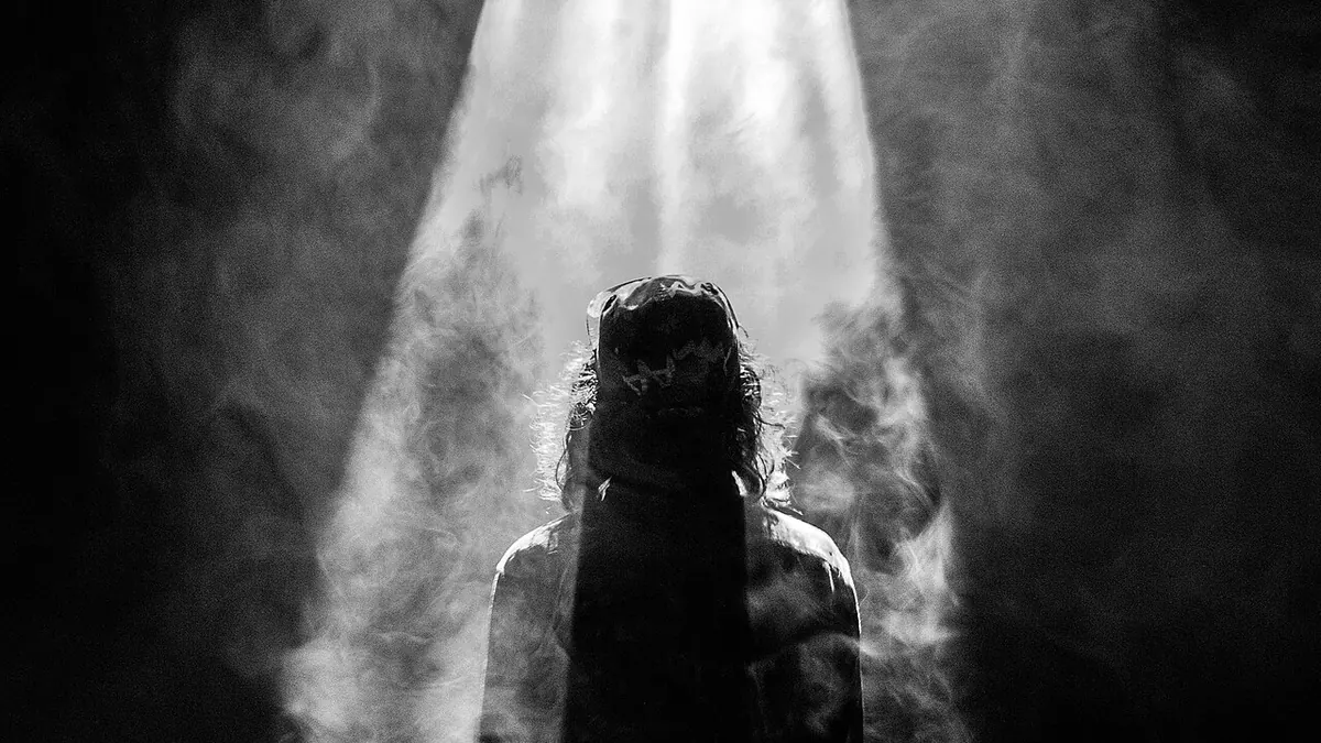 Silhouette seule au centre d'une scène, sous un unique faisceau de projecteur, en noir et blanc