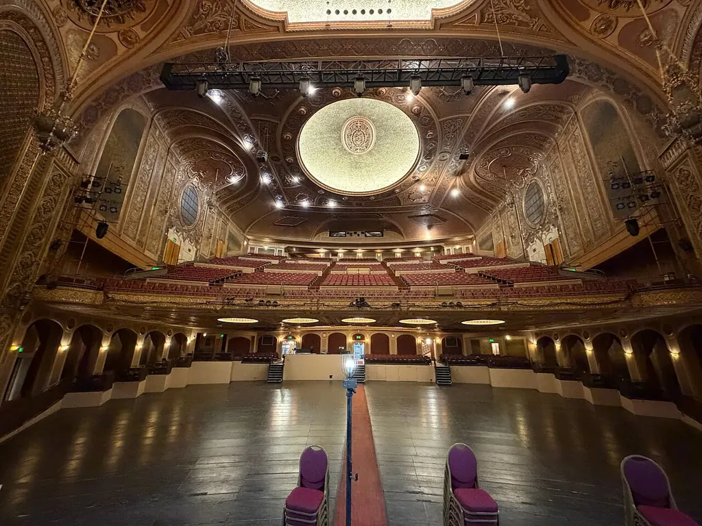 Grande salle de théâtre vide vue depuis la scène, balcons dorés et rangées de fauteuils